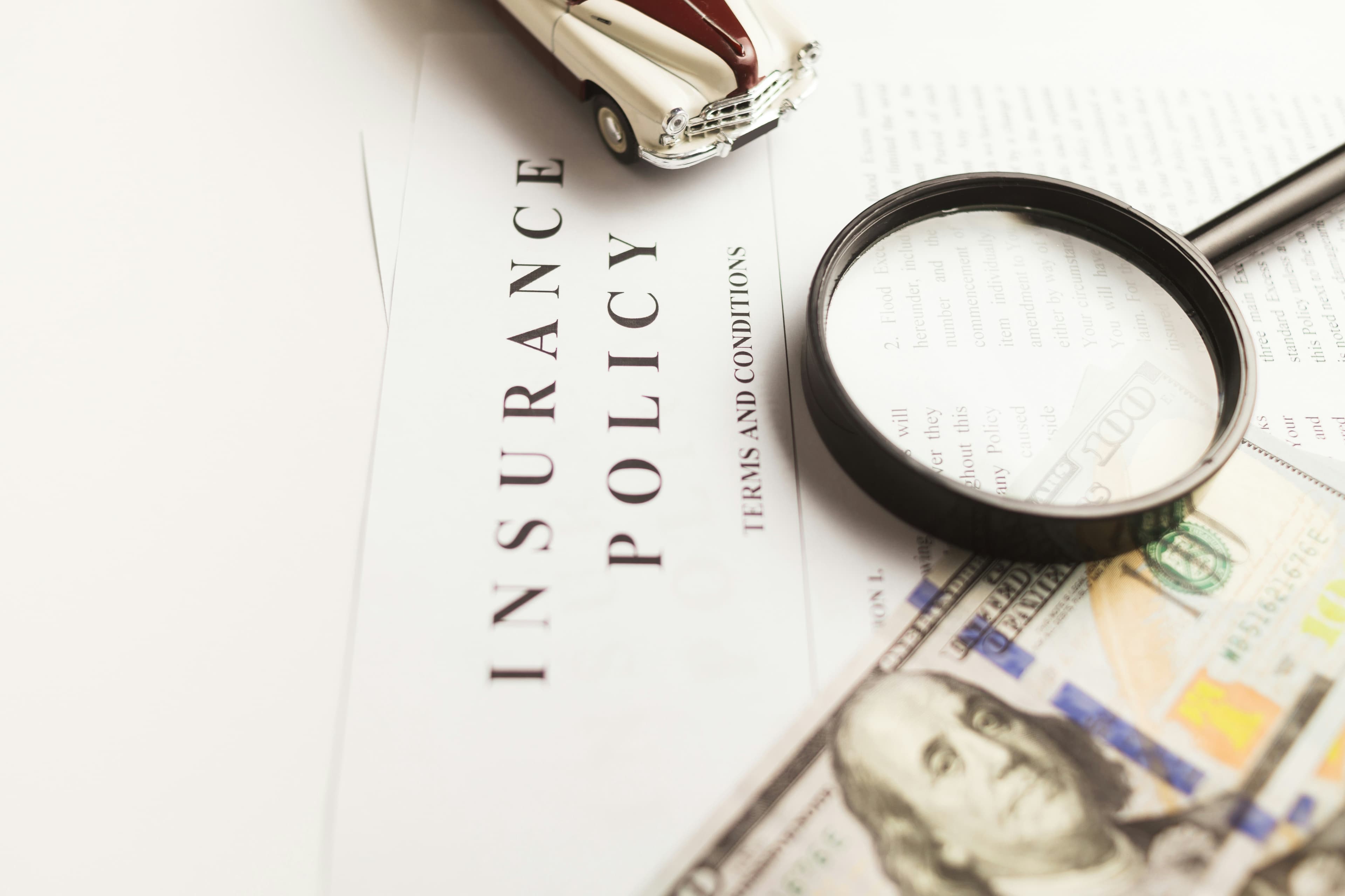 An insurance policy document under a magnifying glass with US currency.